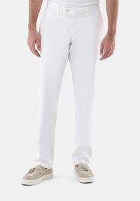 Weiße Hose mit slim-fit, glattem Material, vorderen Taschen und einem diskreten Knopfverschluss, kombiniert mit beigefarbenen Loafers.