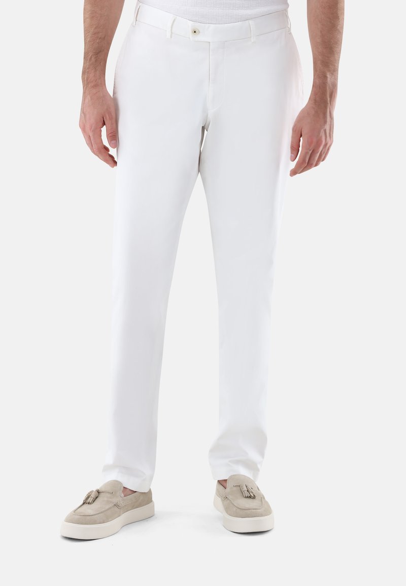 Weiße Hose mit slim-fit, glattem Material, vorderen Taschen und einem diskreten Knopfverschluss, kombiniert mit beigefarbenen Loafers.