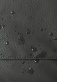 Materiale nero testurizzato con gocce d'acqua sulla superficie, che evidenziano la qualità impermeabile. Presenta una cucitura perdurabilità.