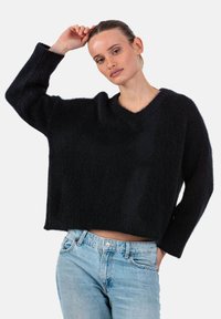 Schwarzer, kurz geschnittener Pullover mit V-Ausschnitt aus weichem, flauschigem Material. Er hat lockere Ärmel und gerippte Bündchen, kombiniert mit hellblauen Jeans.