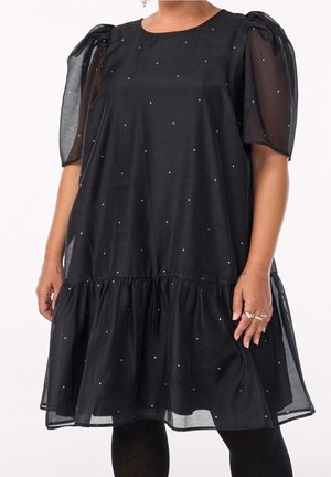 Vestito corto nero con maniche in tulle gonfie e piccoli pois bianchi, indossato con collant neri.