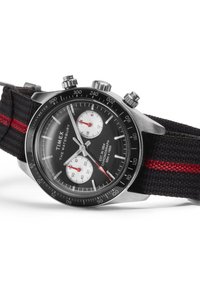 Timex Waterbury pulksteņa korpuss izgatavots no nerūsējošā tērauda, melna ciparnīca, divi balti papildus cipari, sarkani akcenti un melna auduma siksna ar sarkanu joslu.