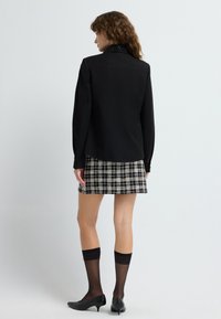 Black long-sleeve shirt with a patterned collar, paired with a plaid skirt in black and white. Black leather low-heeled shoes and sheer black socks.