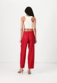 Pantalons rouges taille haute, à jambes larges avec une coupe décontractée et une taille élastique ; associés à un débardeur blanc raccourci. Sandales à talons en bois.