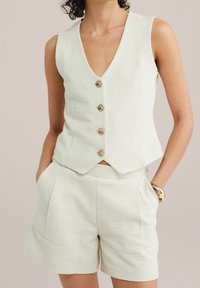 Vitt texturerat väst med djup V-ringning och fem guldtonade knappar, kombinerat med matchande skräddarsydda shorts med sidofickor.