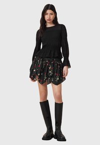 Blusa preta de mangas longas com franzido, combinada com uma saia preta de babados com padrões florais vermelhos. Usada com botas de couro pretas até ao joelho.