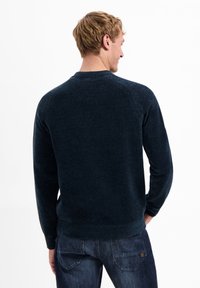 Donkerblauwe gebreide trui met een ronde hals, geribbelde schoudernaden en een snug fit bij de manchetten en de zoom. Zachte textuur en minimaal ontwerp.