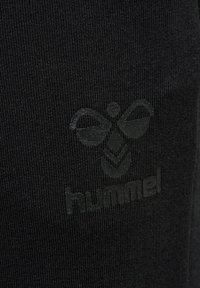 Svart atletisk tyg med en strukturerad logotyp och design med ett bi- och bladmönster, som visar rena linjer och en slät yta.