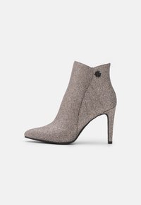 Spidse ankelstøvler lavet af metallisk glimmerstof i nuancer af beige og sølv, med en stilettohælfunktion og en dekorativ sort blomst som accent.
