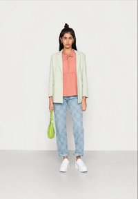 Blazer verde claro, blusa pêssego com laço no pescoço, jeans azul xadrez, ténis brancos e uma pequena mala verde.