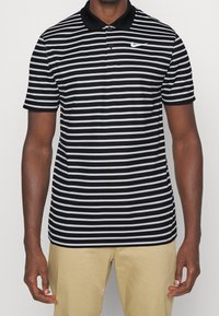 Black and white striped polo shirt with a black collar and Nike logo on the left chest. Short sleeves with flat-knit cuffs.