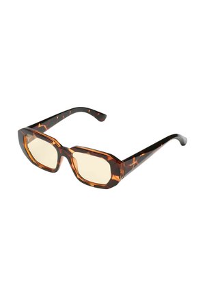 Lunettes de soleil rectangulaires écaille de tortue avec des montures épaisses et des verres teintés de marron clair, inclinées sur un fond blanc.