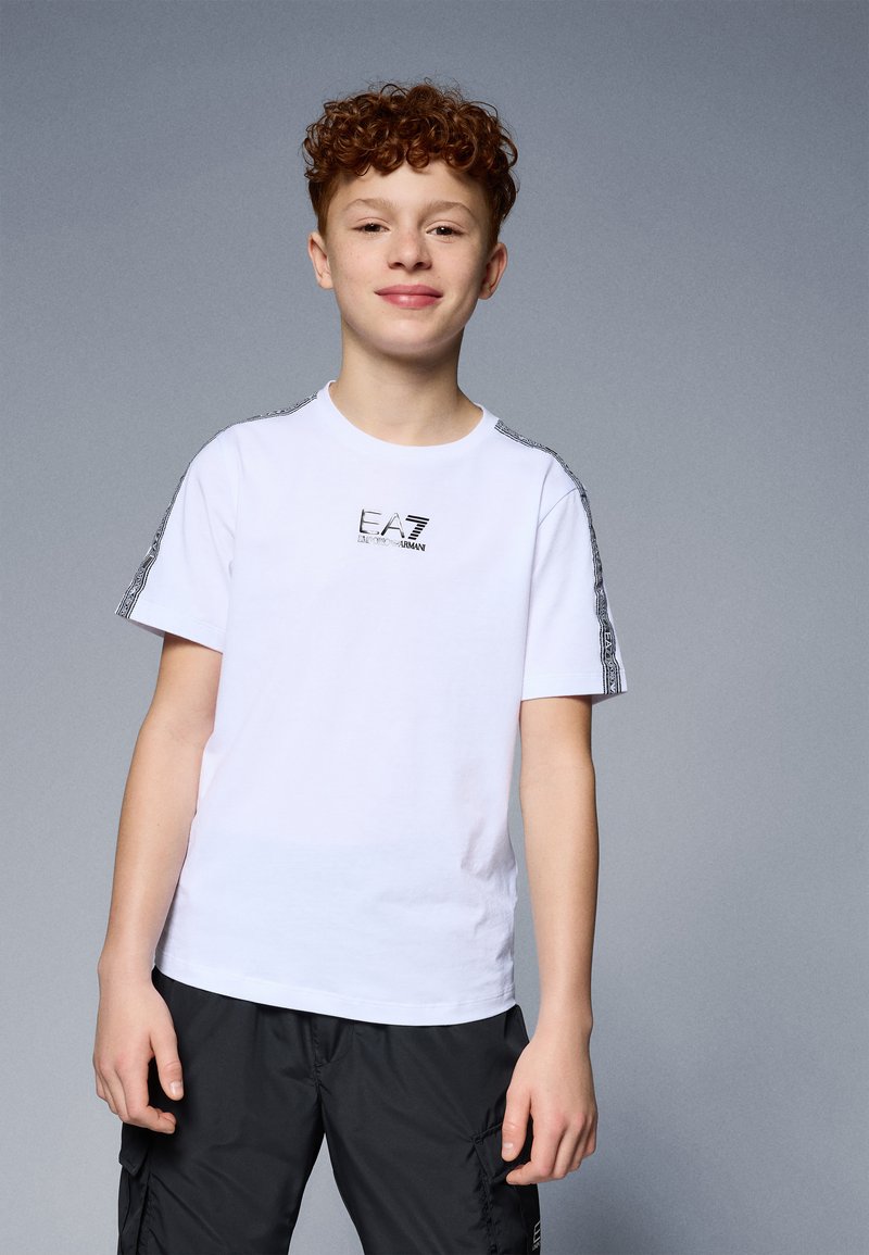 Camiseta blanca de algodón con mangas cortas, cuello redondo y logo negro en el pecho. Acentuada con rayas negras estampadas en los hombros.
