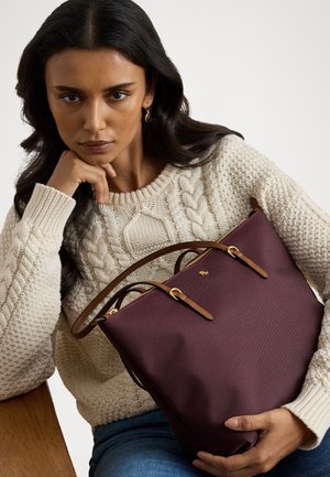 Bordo pirkinių maišas su rudais odiniais akcentais, užtrauktuku uždarymu ir auksinėmis detalėmis. Tekstūruota medžiaga ir struktūrinė forma. Dėvimas su kreminiu megztiniu su pynėmis.