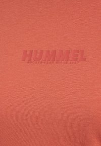 Orange T-shirt med et struktureret "HUMMEL" logo i en mørkere orange nuance, lavet af blødt, ribbet stof.