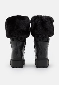 Paire de bottes d'hiver noires avec larges revers en fourrure épaisse, logo embossé sur le talon, tige en tissu à motifs et semelle en caoutchouc épaisse, vue de dos.