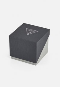 Boîte carrée avec un revêtement texturé gris foncé, une base gris clair et un logo triangulaire sur le dessus. Présente des lignes épurées et un design moderne.