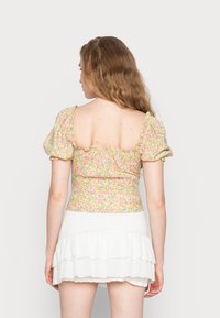 Top curto floral com mangas bufantes em tons de amarelo pastel, rosa e azul. Apresenta um nas costas franzido e um decote quadrado, combinado com uma saia branca com babados.