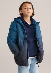 Mėlynas ir tamsiai mėlynas pūkinis švarkas su kapišonu, su siūlėmis apsipinta tekstūra, priekinis užtrauktukas ir šoniniai kišeniai, uždėtas ant tamsiai mėlyno džemperio su kapišonu.