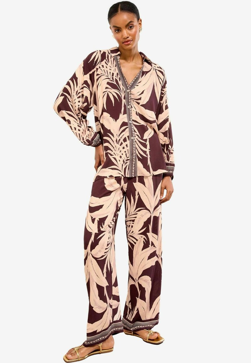 Camicia a maniche lunghe con bottoni e pantaloni a gamba larga di colore marrone scuro con grandi motivi fogliari beige chiaro e rifiniture contrastanti ai polsini e all'orlo.