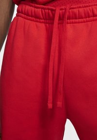 Rode sweatpants met een trekkoord in de taille, zachte textuur en een eenvoudig design. De stof lijkt lichtgewicht en ademend te zijn.
