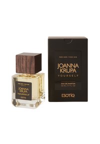 Przezroczysta szklana butelka na perfumy z kwadratową drewnianą zakrętką; oznaczona napisem "JOANNA KRUPA YOURSELF." Czarna opakowanie z złotym nadrukiem. 50 ml.