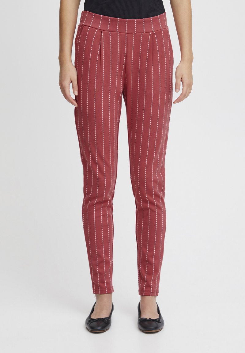 Pantaloni a righe rosse con sottili righe bianche verticali, con pences frontali, forma aderente e texture liscia, abbinati a ballerine nere.