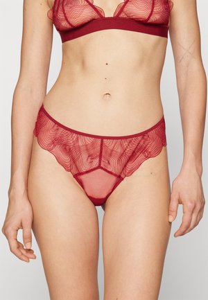 Ensemble de lingerie en dentelle rouge comprenant un bralette transparent avec des motifs tourbillonnants et un pantalon taille basse assorti avec des bords festonnés et des détails géométriques.