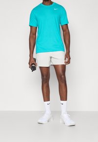 Krótka, morska koszulka Nike z krótkim rękawem w połączeniu z jasnoszarymi szortami, białymi trampkami i białymi skarpetkami z czarnym logo Nike.