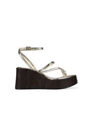 Sandalia de cuña con plataforma de madera oscura y finas tiras metálicas doradas, incluyendo una correa ajustable en el tobillo con una pequeña hebilla.