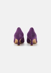 Zapatos de tacón alto de ante púrpura con puntera afilada, tacón fino corto y textura suave. Interior forrado y un diseño sencillo sin patrones.