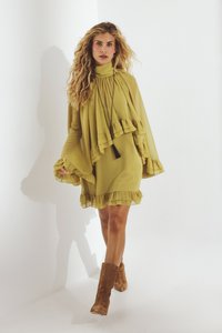 Olīvzaļš kleita ar kārtām un augstu apkakli. Izceļas ar garām piedurknēm un pušķu kaklarotu. Valkāta kopā ar brūnām zamšādām potīšu zābakiem.