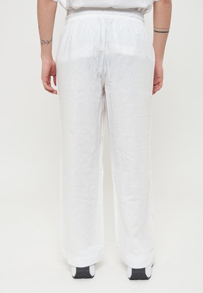 Pantaloni bianchi di lino con una vestibilità comoda, dotati di una cintura elastica e gambe dritte, indossati con scarpe sportive nere.