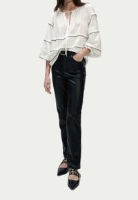 Top blanco texturizado con ribetes negros y escote ceñido. Pantalones de cuero negros con diseño de pierna recta. Bailarinas negras con detalles de tiras.