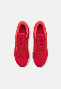 Chaussures de sport rouges avec une tige en maille respirante, des lacets plats et des accents noirs et orange contrastants. Semelle intermédiaire blanche avec une semelle à motifs.