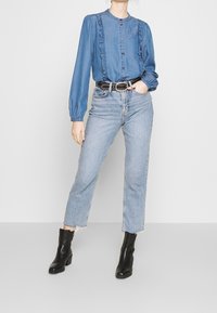 Denim blouse with ruffled edges, long sleeves, and button closure, paired with light-wash straight-leg jeans and black ankle boots.