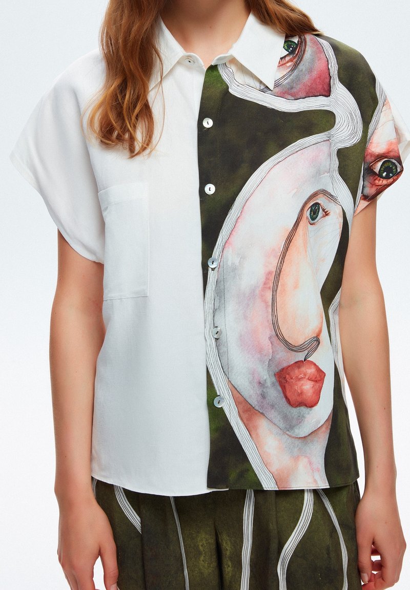 Femme portant une chemise à manches courtes boutonnée avec une moitié blanche et l'autre moitié ornée d'une illustration abstraite de visage.