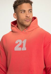 Červená gradientová mikina s kapucí a přední kapsou ve stylu "klokan". Obsahuje velkou bílou grafiku "21". Měkký materiál a detaily se stahovací šňůrkou na kapuce.