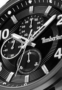 Reloj cronógrafo negro con un dial texturizado, marcadores y agujas plateadas. Presenta tres sub-diales y el logo de Timberland exhibido de manera prominente.