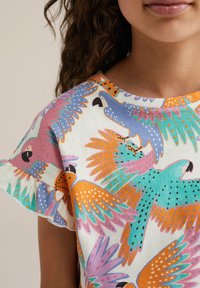 Camiseta de algodón con un estampado colorido de loros en tonos rosa, azul, verde y naranja; textura suave; mangas con volantes; escote redondo.