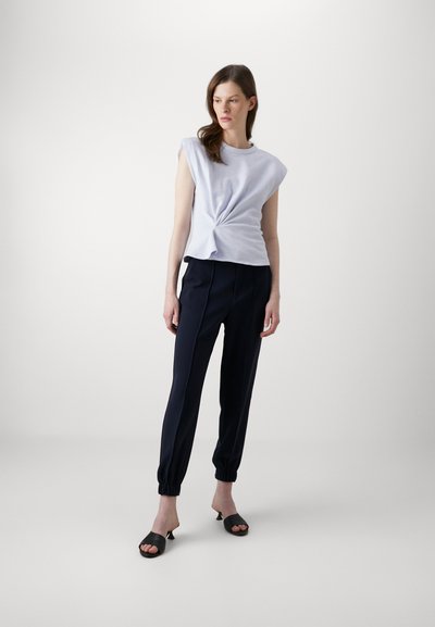 Lichtblauw kortemouwtop met een geknoopte voorkant, gecombineerd met donkerblauwe taps toelopende broek en zwarte open-teen hoge hakken. Eenvoudig ontwerp, zachte textuur.