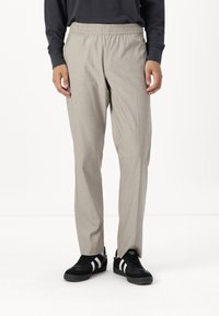 Pantalons enfilés de couleur gris clair, en tissu tiss�é, avec une taille élastique, des jambes fuselées et des poches latérales, portés avec des baskets noires à rayures blanches.
