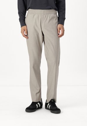 Lys grå, vevde bukser med elastisk midjebånd, avsmalnede ben og sidelommer, brukt med svarte sneakers med hvite striper.