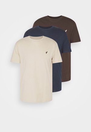 Três t-shirts de gola redonda empilhadas: uma bege, uma azul-marinho escuro e uma castanho escuro. Cada uma apresenta um pequeno logótipos de pássaro bordado no peito.