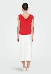 Haut sans manches rouge avec un col drapé, assorti à une longue jupe blanche. Les chaussures sont blanches avec la marque "ONLY" près du talon.