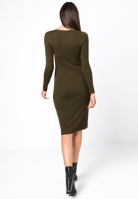 Olivgrön, figurnära stickad klänning med långa ärmar, rundad halsringning och längd till mitten av vaden, ihop med svarta ankelstövlar. Slät textur.