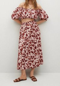 Ensemble de top court décolleté et de jupe maxi florale en rose avec des motifs rouges. Tissu texturé avec taille élastique. Sandales à lanières marron.