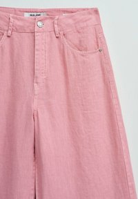 Pantalon en lin rose clair taille haute avec bouton à l'avant, passants pour ceinture, poches avant et étiquette « Salsa Jeans » à la taille.