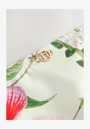 Blommönstrat tyg med rosa och röda blommor på en ljus bakgrund, med en rund knapp i guld och detaljer i vit tråd.