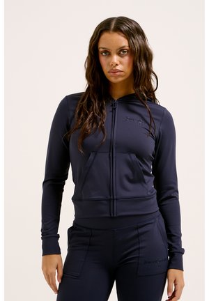 Navy zip-up hoodie in stretch fabric with kangaroo pockets, ribbed cuffs, and embroidered logo detail on the chest. Soft texture.
